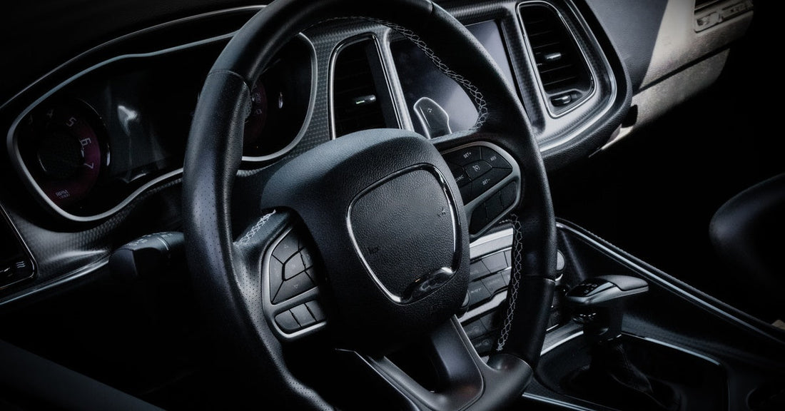 A close-up of a black, leather-covered steering wheel set in the all-black interior of a luxury vehicle.