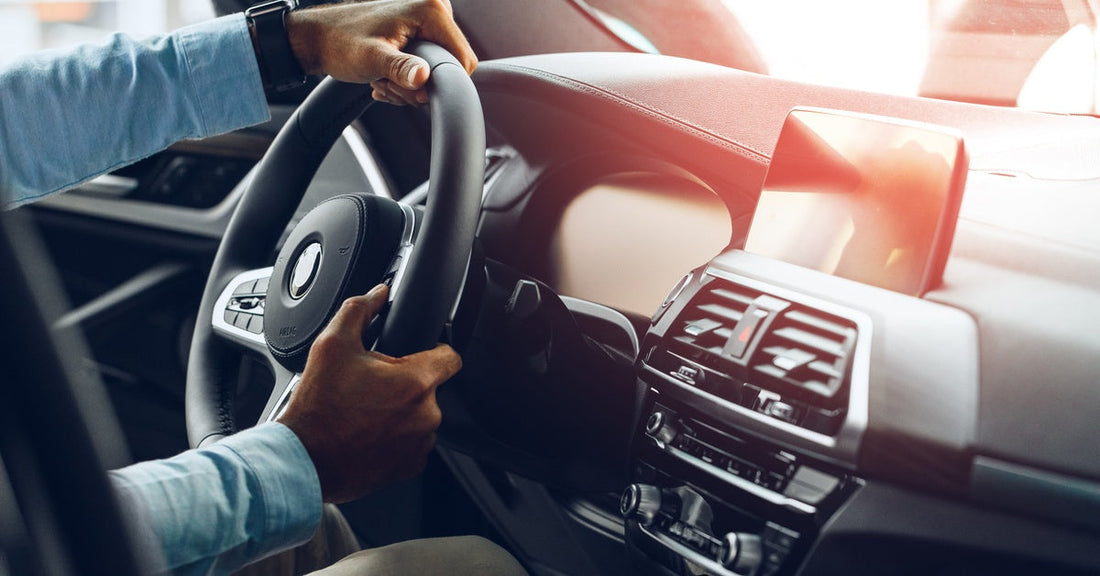A close-up of a man, who's wearing a dress shirt and a watch, holding the steering wheel of a car while driving.