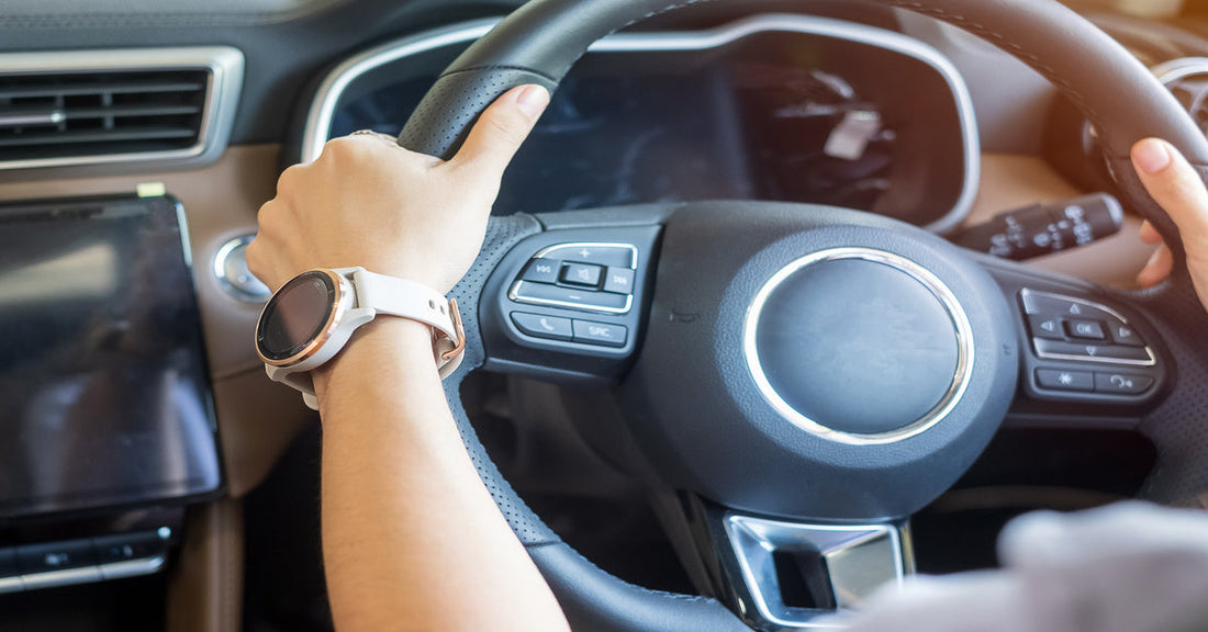 A person’s hands gripping a steering wheel safely at 10:00 and 2:00. The person has a smart watch on their left wrist.